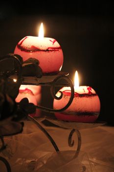 A curved metal candle holder set on a table covered with netting. Soft pink light is emitted from the lit candles.