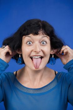 woman sticking out her tongue and pulling her ears - isolated on blue