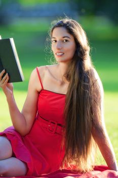 woman with long hair in red dress reading a book in a park