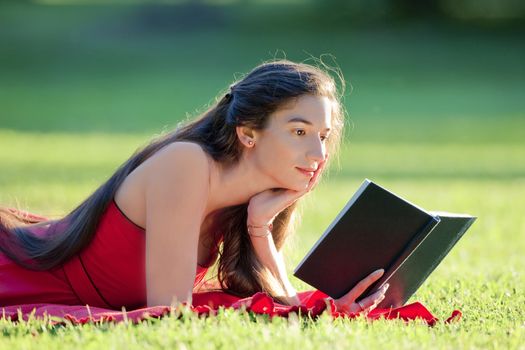 woman with long hair in red dress reading a book in a park