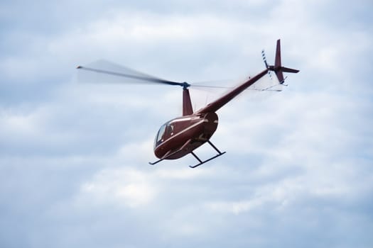small brown helicopter in blue cloudy sky