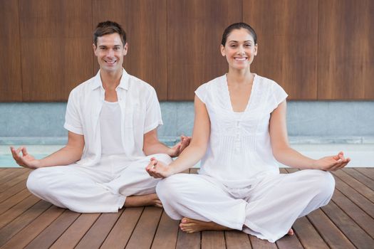 Attractive couple in white sitting in lotus pose smiling at camera in health spa