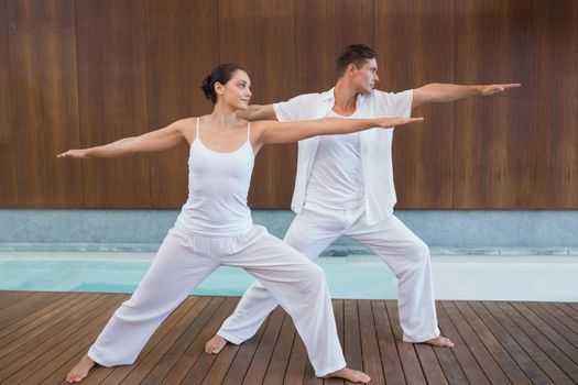 Peaceful couple in white doing yoga together in warrior position in health spa