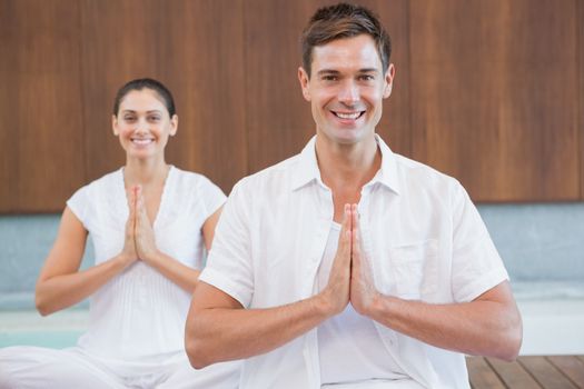 Peaceful couple in white sitting in lotus pose together in health spa