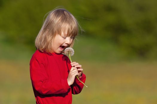 boy with long blond hair holding dandelion standing in a field