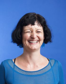 portrait of middle-aged woman with dark hair laughing - isolated on blue