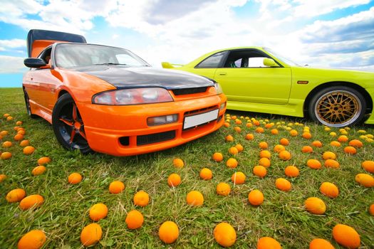 Two bright colour cars and fruit on grass
