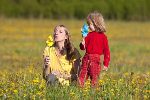 mother and son playing with pinwheels in a dandelion field