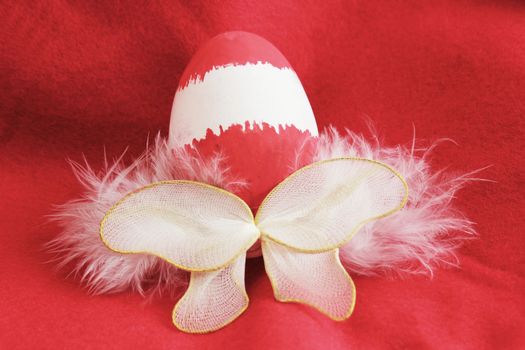 Red and white painted Easter egg, with white fairy wings attached to it, on a red fleece background. 
