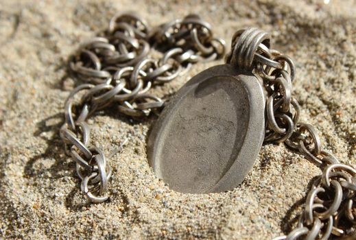 A rustic steel metal photo locket with chain, lying in sand. The pendant is blank and the space can be used to insert text or image. Suitable for concepts like - finding treasure, 
