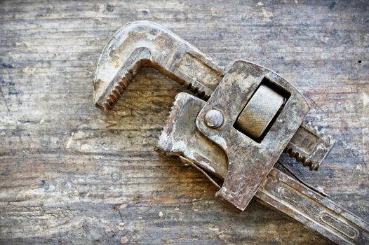 An old rustic pipe plumbing wrench lying on an old wood plank
