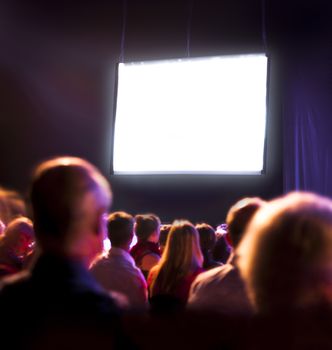 Crowd audience in dark looking at bright screen