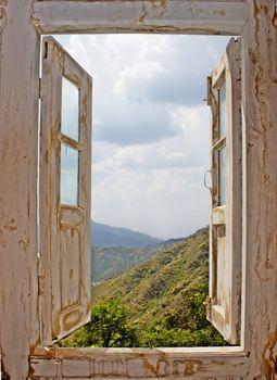 View of the mountains and clouded sky from an open old white wood window. Ideal for concepts related to outdoors, nature, exploration, peace, and inspiration.
