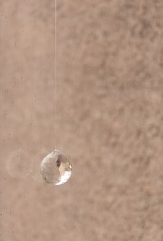 Crystal ball hanging in rainy window with rough cast wall behind. Interior detail.