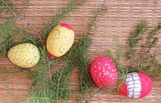 Easter Sunday decoration with yellow and red painted Easter eggs placed amidst fir twigs on a bamboo mat background
