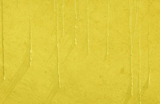A yellow concrete plastered wall with paint drip texture. This vibrant colored wall will serve as a great background texture. 
