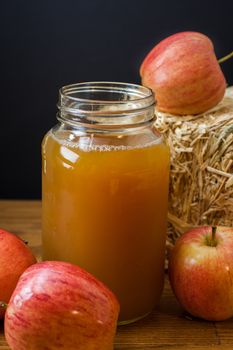 Fresh pressed apple cider and apples on a wooden table with a hay bale in the background.
