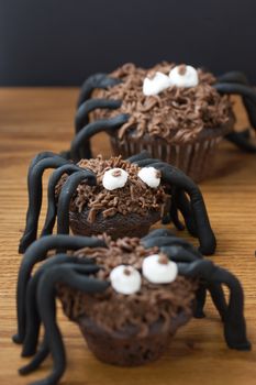 Chocolate cupcake spiders on a wooden surface with a bale of straw in the background.
