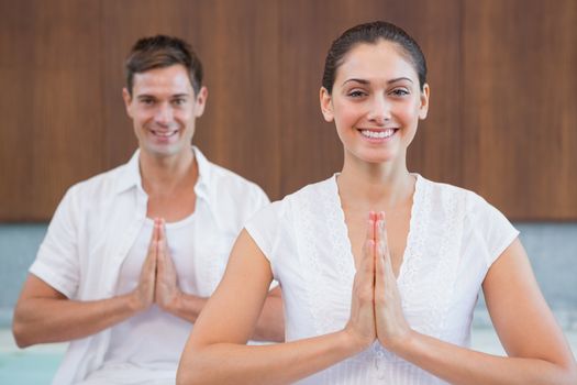 Smiling couple in white sitting in lotus pose with hands together in health spa