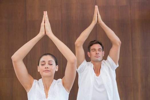 Peaceful couple in white doing yoga together with hands raised in health spa