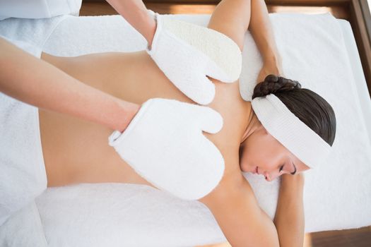 Beauty therapist rubbing womans back with heated mitts in the health spa