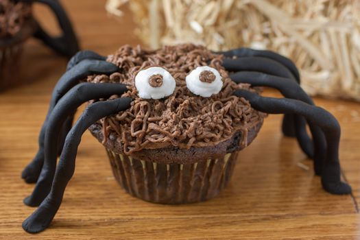 Chocolate cupcake spiders on a wooden surface with a bale of straw in the background.