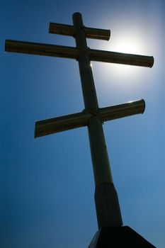 High brilliant metal cross against the solar sky