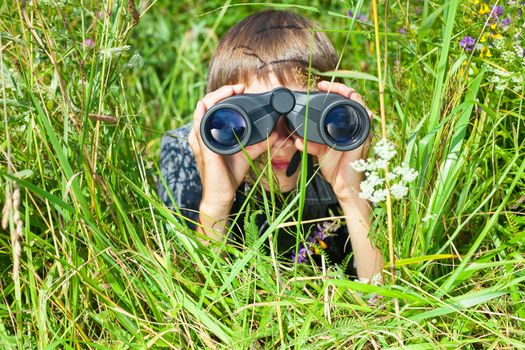 Boy hiding in grass looking through binoculars outdoor
