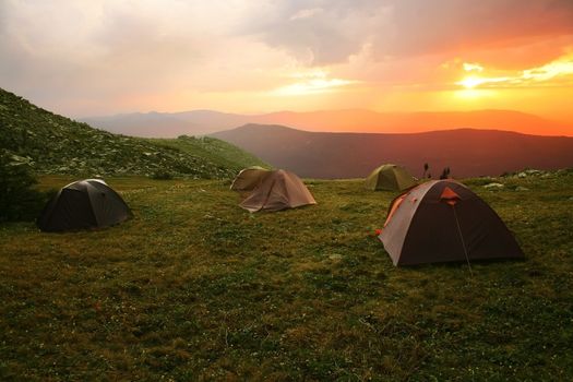 Mountain landscape with sunset and tents on glade