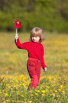 boy with long blond hair playing with pinwheels on a dandelion meadow