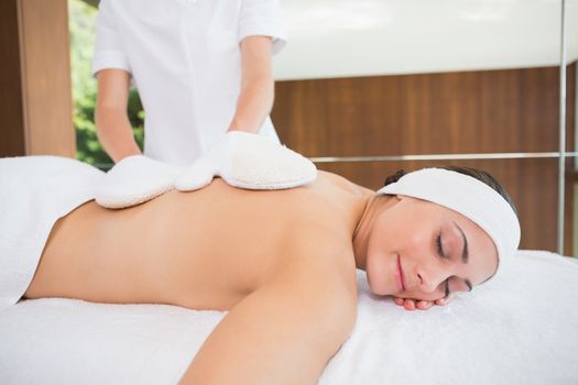 Beauty therapist rubbing womans back with heated mitts in the health spa