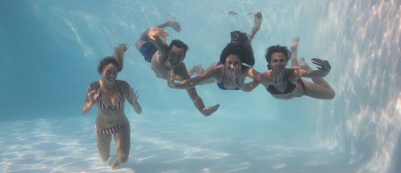 Smiling friends looking at camera underwater in swimming pool on their holidays