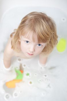 boy with long blong hair standing in bathtub looking up