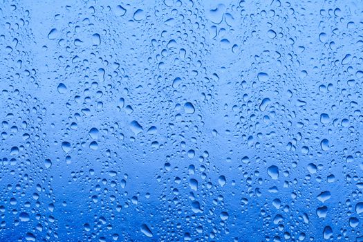 closeup of waterdrops after rain on glass roof reflecting blue sky