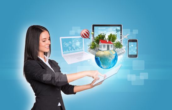 Beautiful businesswomen in suit using digital tablet. Earth with buildings and laptop, tablet and smartphone. Element of this image furnished by NASA