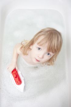 boy with long blond hair playing with plastic boat in bathtub