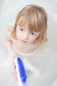 boy with long blond hair playing with plastic boat in bathtub