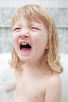 boy with long blond hair sitting in bathtub, screaming