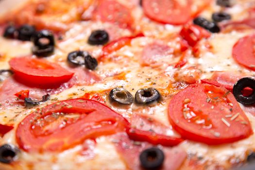 Close-up shot of delicious Italian pizza with ham, tomatoes and olives, selective focus  