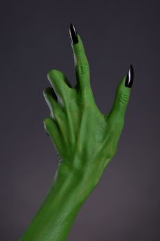 Green witch hand with black nails, Halloween theme, studio shot on black background 