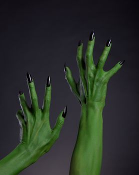 Green witch hands with black nails stretching up, Halloween theme, studio shot on black background 