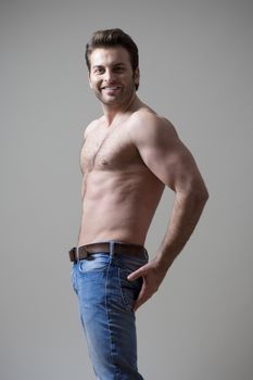 young shirtless musculous man in jeans smiling - isolated on gray