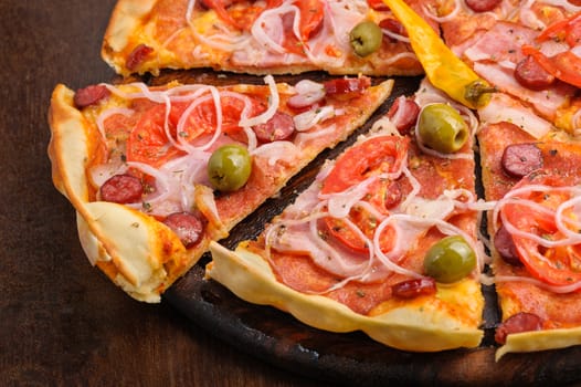 Closeup of pizza with tomato, salami, peppeeoni, olives and yellow hot pepper