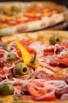 Macro closeup of pizza with tomato, salami, peppeeoni, olives and yellow hot pepper