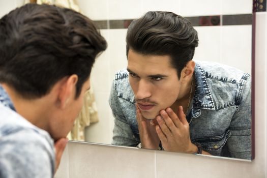 Close Up of Young Man Examining Face in Reflection of Mirror and Glaring at Self
