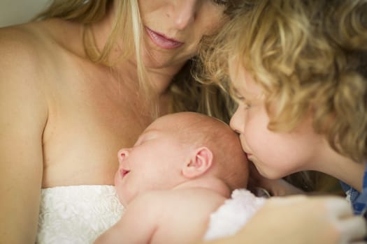 Beautiful Young Mother Holds Newborn Baby Girl as Brother Kisses Her Head.