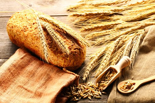 Rye spikelets and bread on wooden background