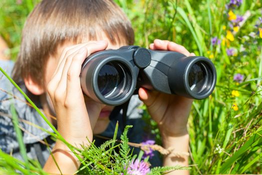 Boy hiding in grass looking through binoculars outdoor