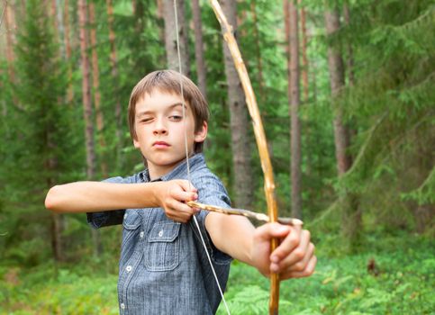 Boy aiming home-made wooden bow outdoors