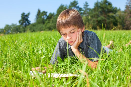 Boy lying in grass reading a book in a summer field